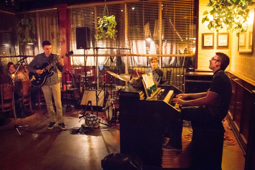 Photo of Henry Dickhoff playing organ with trio in restaurant, along with guitarist and drummer.