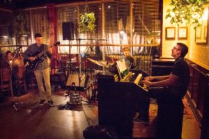 Photo of Henry Dickhoff playing organ with trio in restaurant, along with guitarist and drummer.